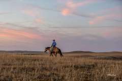 Cowboy riding across the grasslands at sunset